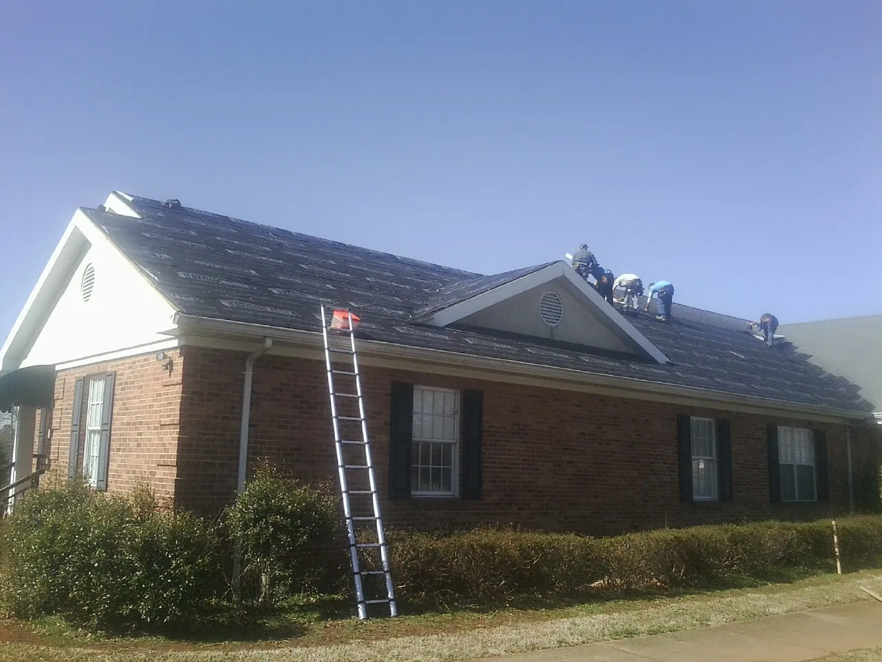 Crew tearing shingles off a brick ranch roof with a ladder set — Metal Roof Repair work by our crew in Tatamy