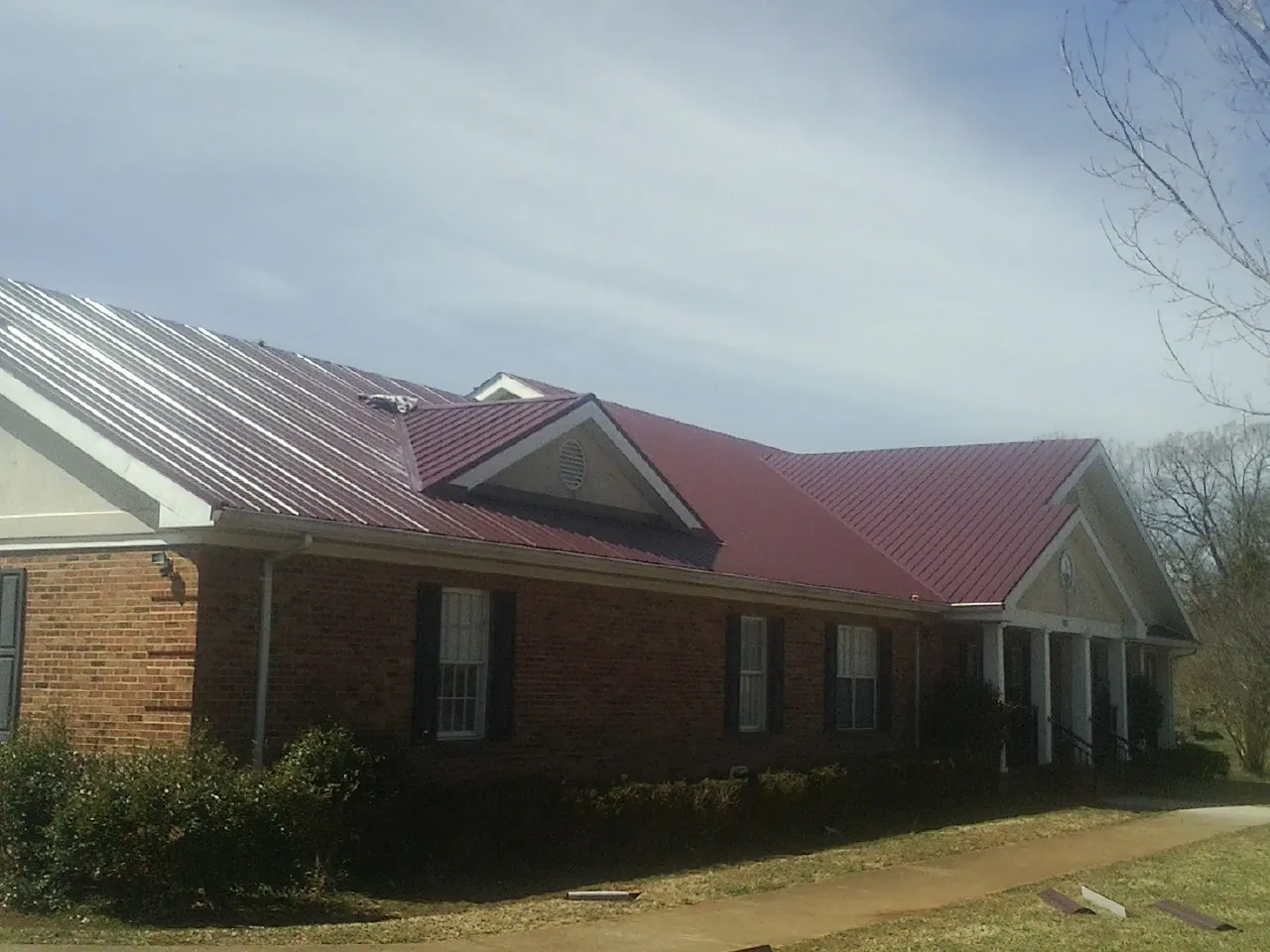Red metal roof with gabled entries on a long brick building, from a Hail Damage Roof Repair job in Tatamy