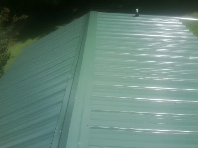 New green metal panels meeting at the ridge of a roof — Flat Roof Repair work by our crew in Tatamy