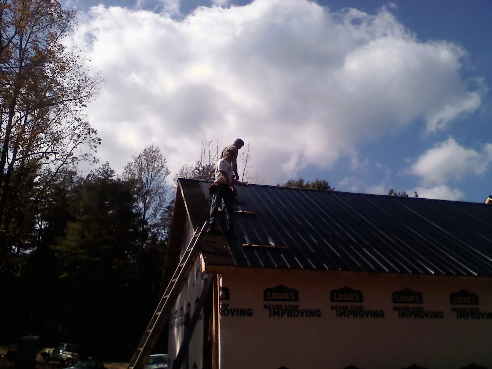 Roofer fastening dark metal panels high against a cloudy sky, from a Roof Inspection job in Tatamy