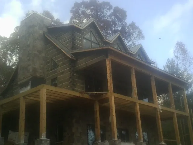 Stone chimney and dormers on a large log home with a timber porch in Tatamy