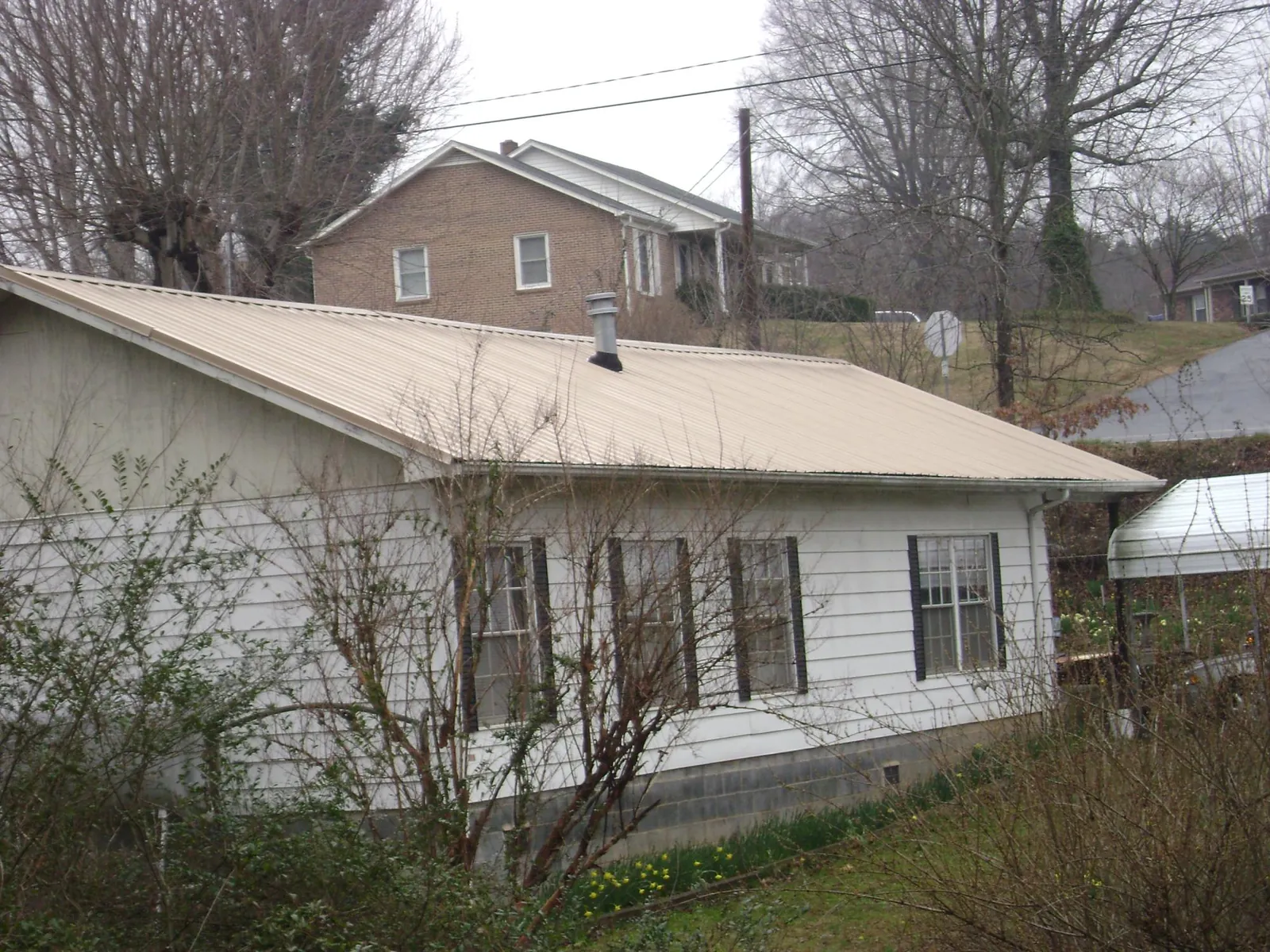 Tan metal roof on a white sided house set into a hillside — Commercial Roofing by Roofing Brothers in Tatamy